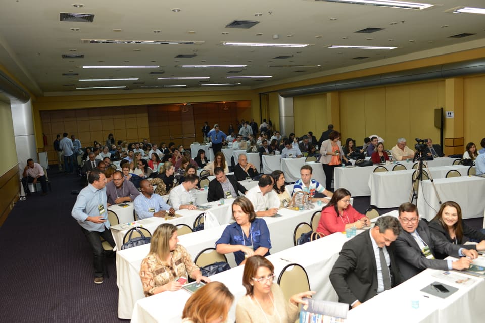 Vista elevada de participantes com crachás sentados em mesas compridas durante um evento de capacitação.