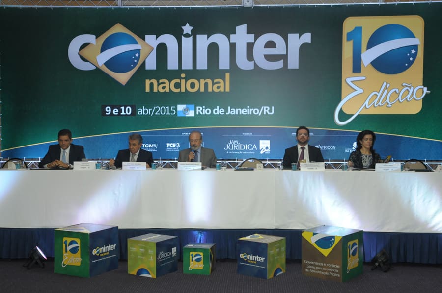 Mesa de abertura com seis pessoas sentadas diante do painel do congresso, uma delas falando ao microfone.